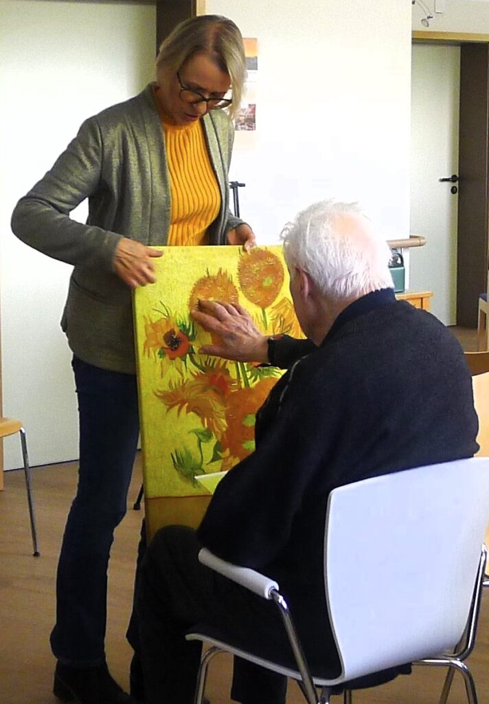 Petra Kellermann betrachtet mit einem Teilnehmer ein Bild mit gelben Blumen.